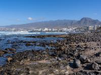 An felsigem Küstenabschnitt bei Playa de las Americas mit Blick zu den Bergen